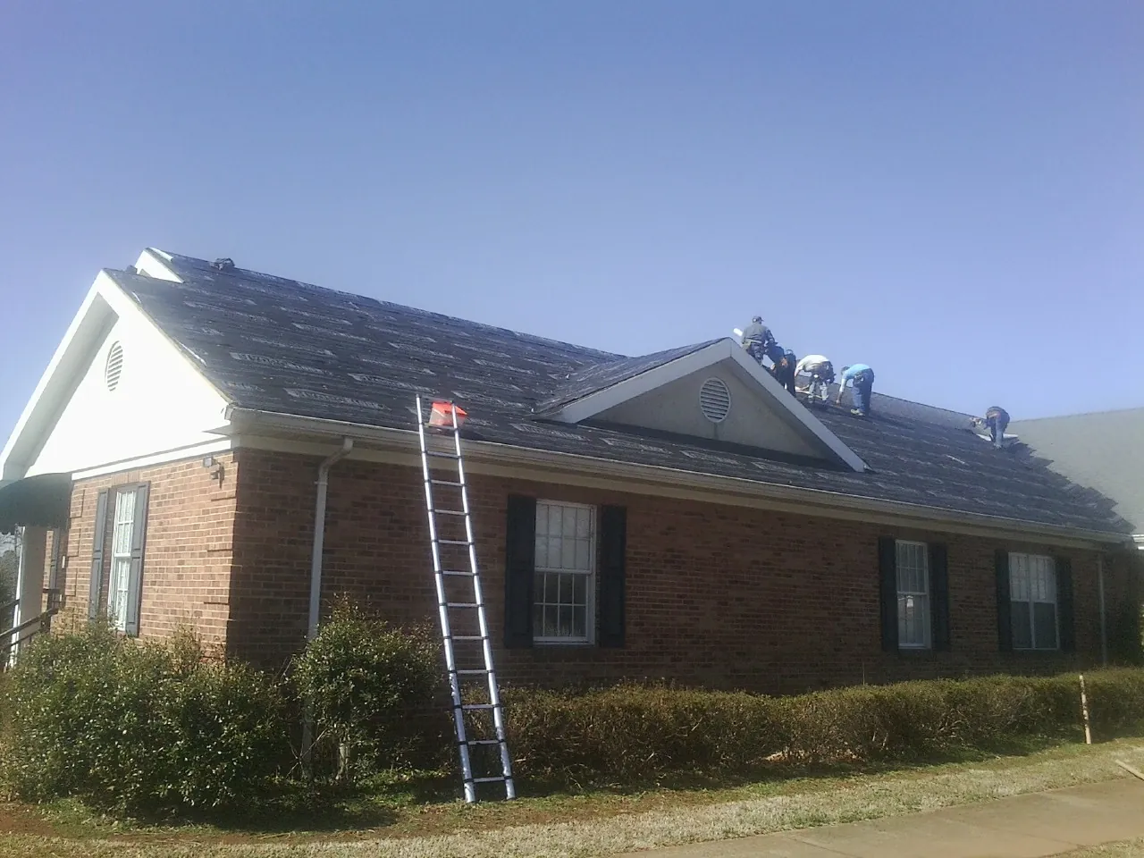 Crew tearing shingles off a brick ranch roof with a ladder set — Metal Roof Repair work by our crew in Casstown