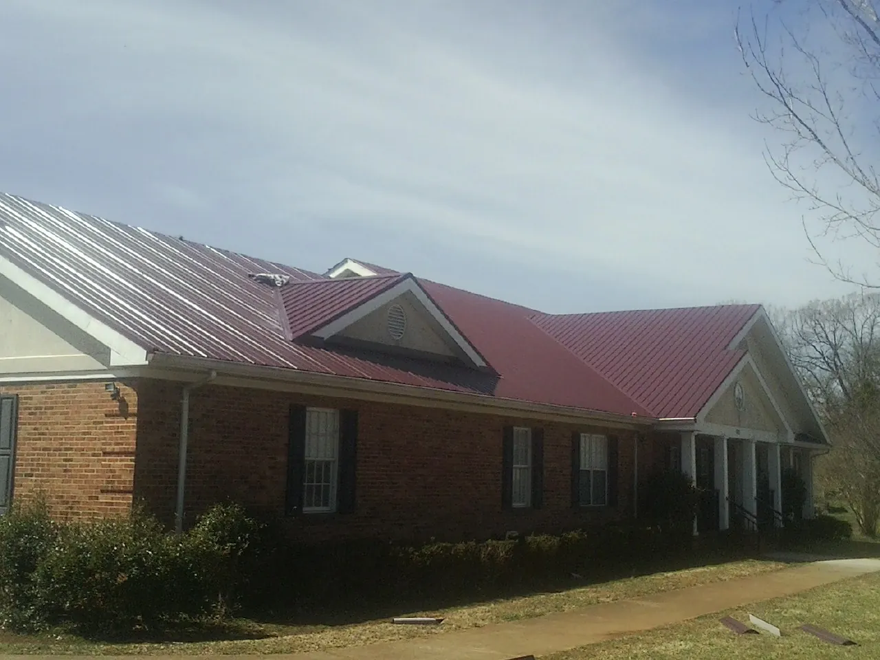 Red metal roof with gabled entries on a long brick building, from a Hail Damage Roof Repair job in Casstown