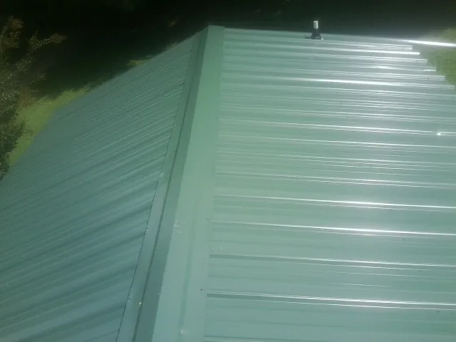 New green metal panels meeting at the ridge of a roof — Flat Roof Repair work by our crew in Casstown