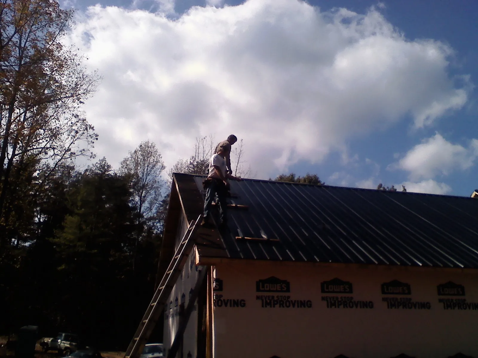 Roofer fastening dark metal panels high against a cloudy sky, from a Roof Inspection job in Casstown