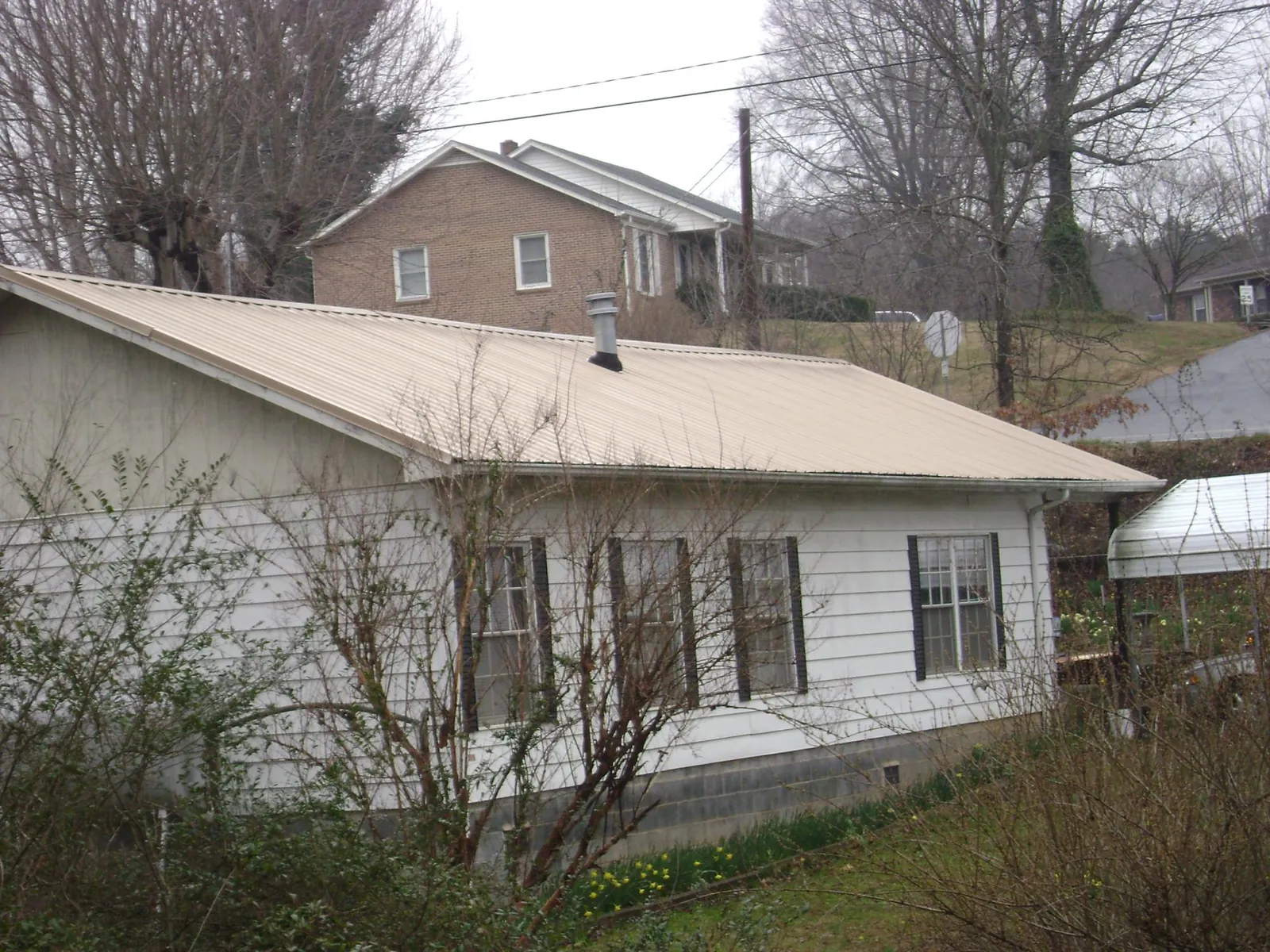 Tan metal roof on a white sided house set into a hillside — Commercial Roofing by Roofing Brothers in Casstown